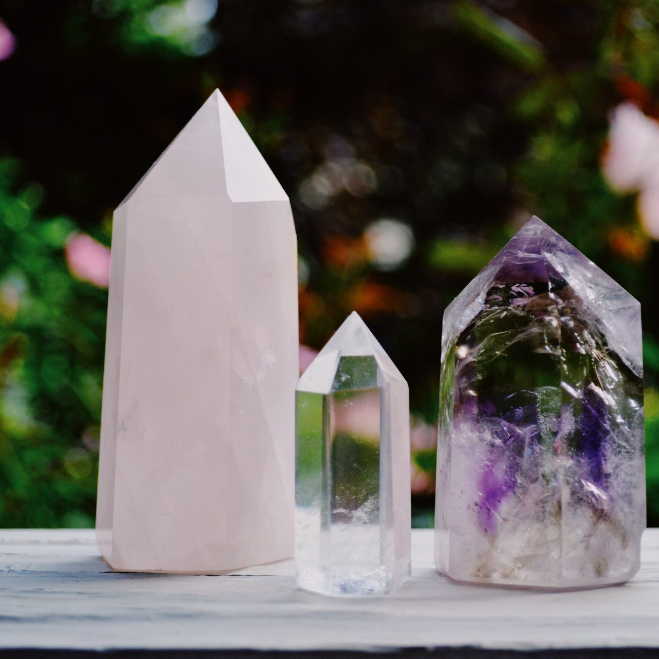 Trois cristaux de formes pyramidales, en quartz rose, cristal transparent et améthyste.